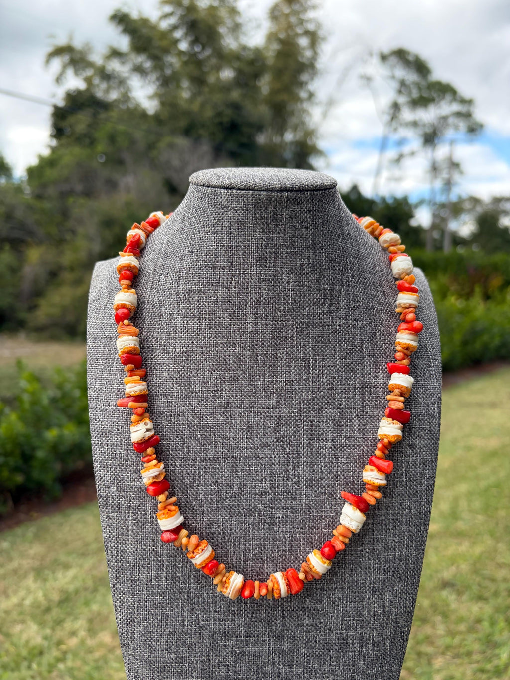 May include: A beaded necklace featuring a repeating pattern of irregular, tumbled red coral pieces, small orange coral fragments, and cylindrical white shell beads strung together to form a continuous circular strand of organic textures.